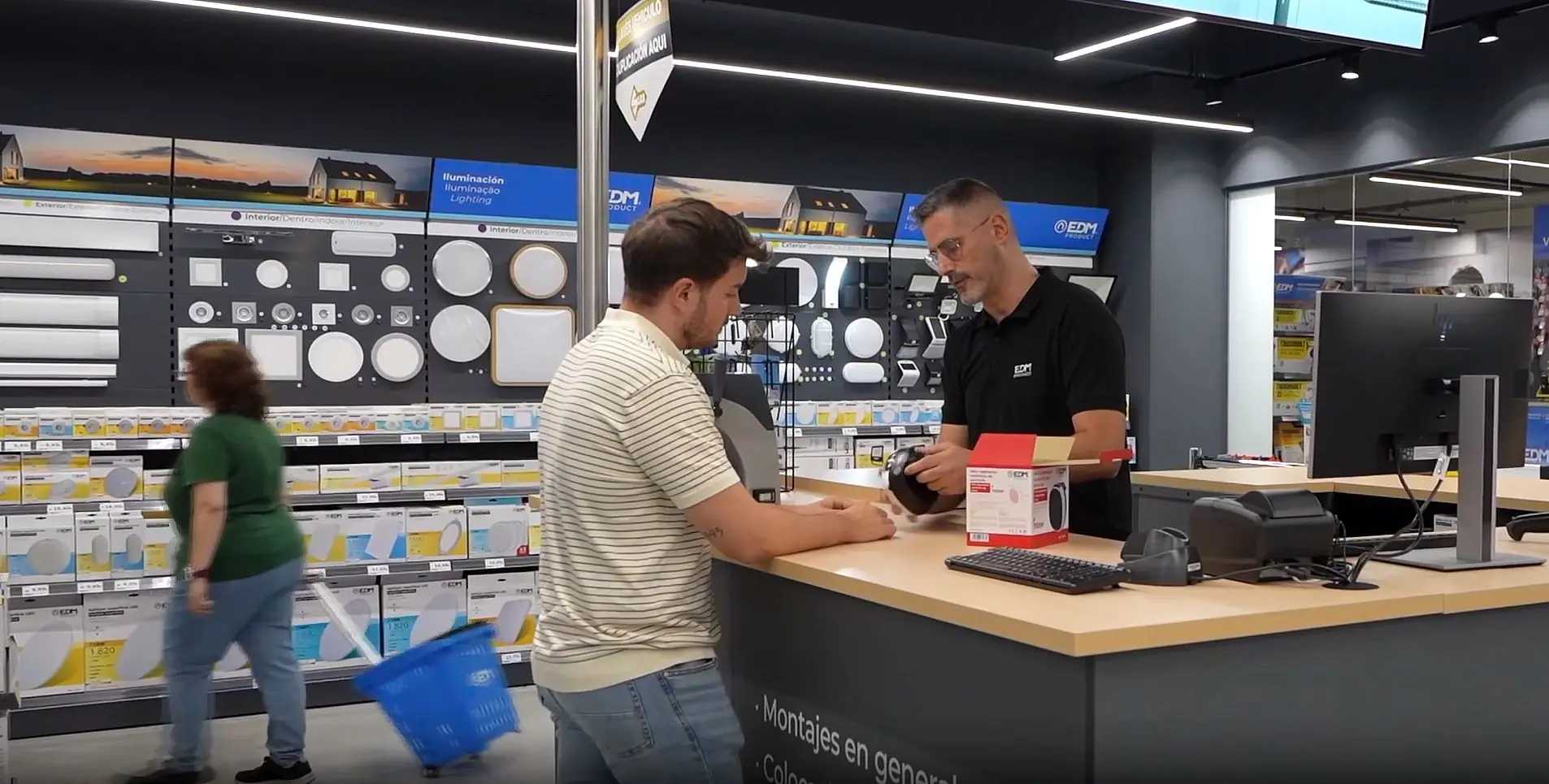 Profesional de Elektro3 atendiendo a un cliente en el mostrador del showroom, junto al lineal de iluminación